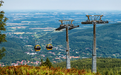Seilbahn über bewaldetem Tal mit Ausblick auf Dorf und Landschaft.