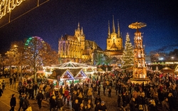 Menschen auf einem beleuchteten Weihnachtsmarkt in Erfurt bei Nacht.