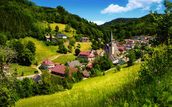 Panoramablick auf ein Dorf in einer hügeligen, grünen Landschaft mit Kirche im Zentrum.