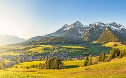 Panorama einer Berglandschaft mit grünen Wiesen und einem kleinen Dorf.