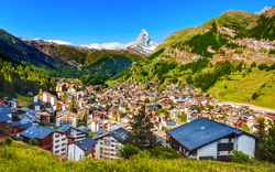 Blick auf ein Bergdorf umgeben von grünen Hügeln und Bergen.