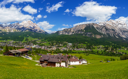 Alpenpanorama mit grüner Wiese, Dorf und Bergen unter blauem Himmel.