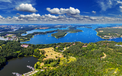 Luftaufnahme von Seenlandschaft mit Booten und Wäldern unter blauem Himmel mit Wolken.