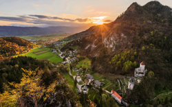 Ländliche Idylle bei Sonnenuntergang mit Burg und Bergen im Hintergrund.
