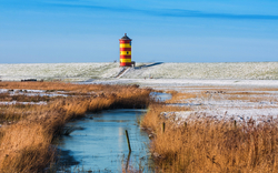 Leuchtturm in schneebedeckter Landschaft an der ostfriesischen Küste im Winter.