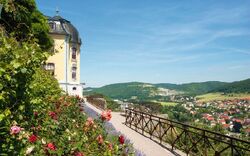 Gelbes Schloss neben Garten mit Blick auf eine Landschaft und ein Dorf.