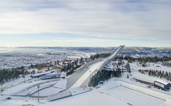 Holmenkollen-Skisprungschanze in Oslo im Winter mit verschneiter Landschaft im Hintergrund.