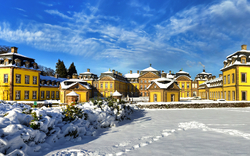 Gelbes Barockschloss im Schnee mit blauem Himmel.