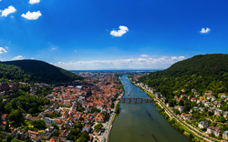 Luftaufnahme einer Stadt mit Fluss, Brücke und umgebenden bewaldeten Hügeln.