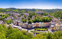 Panoramablick auf eine Stadt in einem grünen Tal, umgeben von bewaldeten Hügeln.