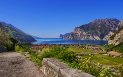 Blick auf den Gardasee mit umliegenden Bergen und einem Dorf im Vordergrund.
