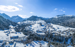 Verschneite Berglandschaft mit Dörfern und bewaldeten Hängen unter blauem Himmel.