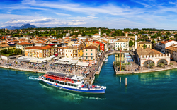 Panoramablick auf die Altstadt und den Hafen von Lazise am Gardasee in Italien, umgeben von blauem Wasser, mit sichtbaren Schiffen und Booten.