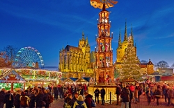 Menschen auf einem festlichen Weihnachtsmarkt bei Nacht mit Lichtern und Attraktionen.