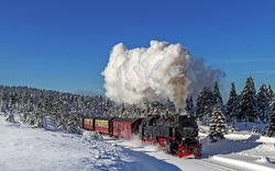 Dampflokomotive zieht Zug durch verschneite Winterlandschaft.