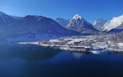 Panoramablick auf den Achensee und die umliegenden, schneebedeckten Berge und Dörfer unter klarem, blauem Himmel im Winter.