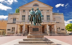 Denkmal von Goethe und Schiller vor dem Deutschen Nationaltheater in Weimar an einem sonnigen Tag.