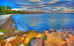 Küste mit blauem Meer, Felsen und bewölktem Himmel bei Sonnenuntergang.