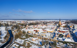 Verschneite Stadt mit Kirche, Fluss und blauem Himmel aus der Vogelperspektive.