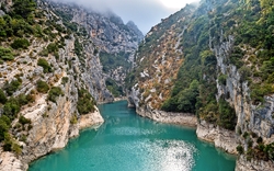 Blick auf eine malerische Schlucht mit türkisblauem Wasser und grünen, bewaldeten Hängen.