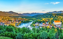 Panoramablick auf eine Stadt mit Fluss, umgeben von Bergen und Wäldern bei Sonnenaufgang.