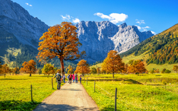 Berglandschaft im Herbst mit Wanderern auf einem Weg und bunten Bäumen.